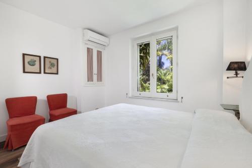ein weißes Schlafzimmer mit einem weißen Bett und zwei roten Stühlen in der Unterkunft Estate4home- Villa Le Camelie in Sant'Agnello