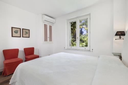 a white bedroom with a white bed and two red chairs at Estate4home- Villa Le Camelie in Sant'Agnello