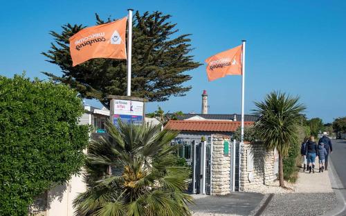 twee oranje vlaggen voor een gebouw met palmbomen bij Camping Les Perouses in Saint-Clément-des-Baleines