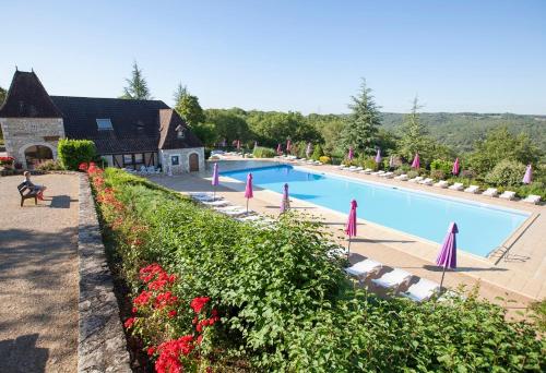 a large swimming pool with pink umbrellas and red flowers at Camping Domaine de la Paille Basse - Maeva in Souillac
