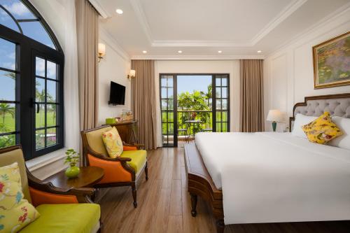 a hotel room with a large bed and a chair at Maison Fleur Luxury Hoi An in Hoi An