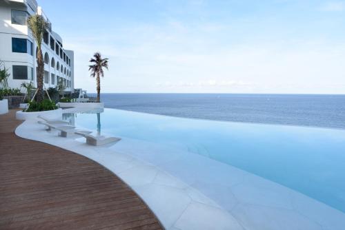 a pool with a table and benches next to the ocean at Royal Avila Boutique Resort in Senggigi 