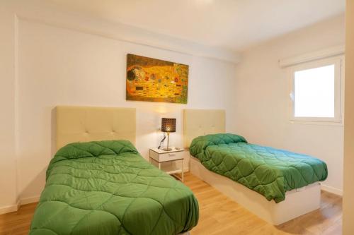 two beds in a white room with green comforter at Seafront Marina 1 Apartment in Pollença