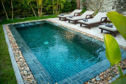 a swimming pool with chaise lounges and chairs in a backyard at Le Chanthou Boutique in Siem Reap