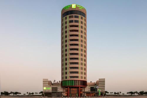 a tall building with a green sign on it at Holiday Inn & Suites - Dubai Science Park by IHG in Dubai