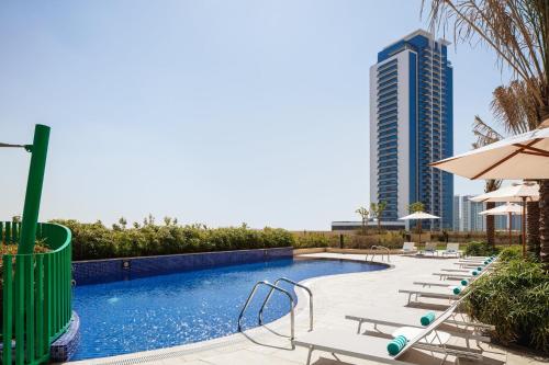 une piscine avec des chaises et un grand bâtiment dans l'établissement Holiday Inn & Suites - Dubai Science Park, an IHG Hotel, à Dubaï