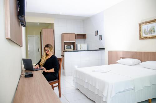 a woman sitting in a chair with a laptop in a bedroom at Hotel Acarau Riviera in Acaraú