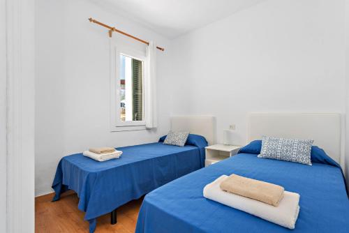 two beds in a room with blue sheets and a window at Apartamento Can Harmonia - Arenal den Castell in Arenal d'en Castell