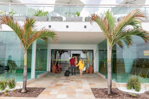 a man and woman walking into a building with palm trees at Yak Beach Hotel Natal in Natal