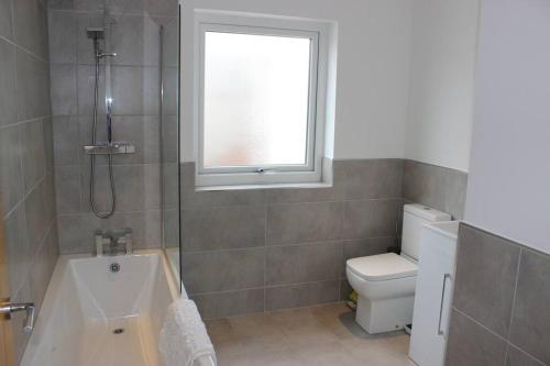 a bathroom with a tub and a toilet and a window at The White House in Wirral