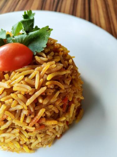 a plate of rice with a tomato and greens at Mohammadia Restaurant & Guest House in Dhaka