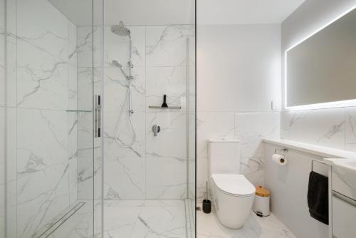a white bathroom with a shower with a toilet at Oceanside Apartment with Iconic Views in Mount Maunganui