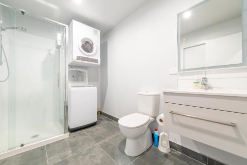 a white bathroom with a toilet and a shower at Deluxe One Bedroom Apartment in Newmarket Auckland in Auckland