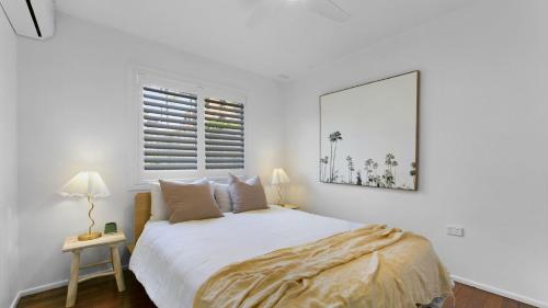 a white bedroom with a bed and a window at Malolo in Yamba