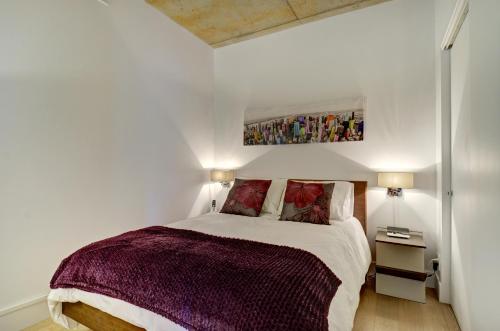 Dormitorio blanco con cama con manta morada en Les Immeubles Charlevoix - Le 760404, en Quebec