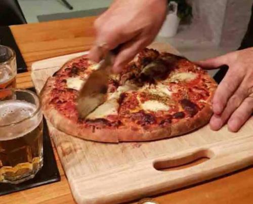 a person cutting a pizza on a wooden cutting board at Family Tides Beach House in Rosebud