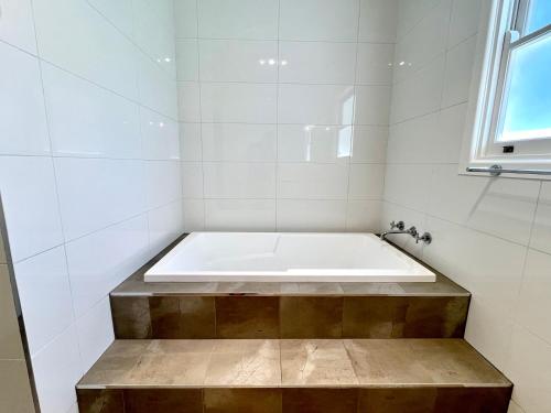 a bath tub in a white tiled bathroom at Walnut House Mildura in Mildura