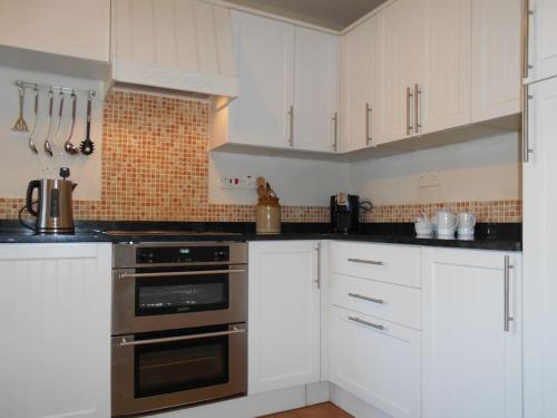 a kitchen with white cabinets and stainless steel appliances at The Granary, Old Corn Mill, Yorkshire Dales in West Burton