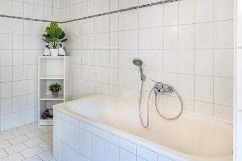 a bath tub with a shower in a white tiled bathroom at Haus Steinatal in Ühlingen-Birkendorf