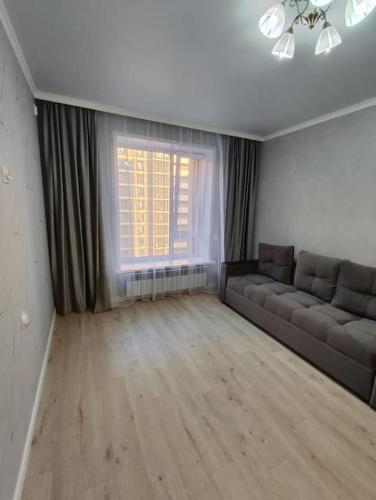 a living room with a couch and a window at Квартира в ЖК Будапешт 10 мин от Аэропорта и ЭКСПО in Prigorodnyy