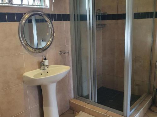 a bathroom with a sink and a shower with a mirror at Edwaleni Guest Lodge in Pinetown