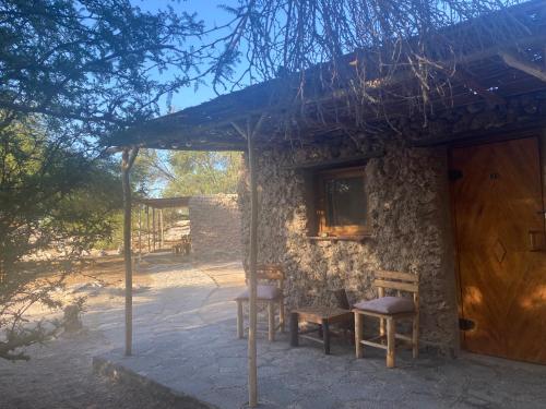 Casa de piedra con 2 sillas y puerta de madera en El Huarango Eco retreat, en La Huaica