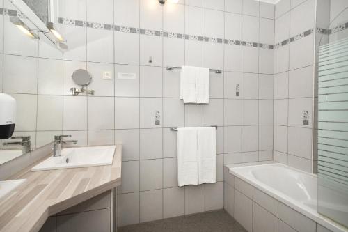 een witte badkamer met een bad en een wastafel bij Logis Hôtel du Centre - Halte idéale en cyclotourisme avec garage à vélos clos in Molsheim