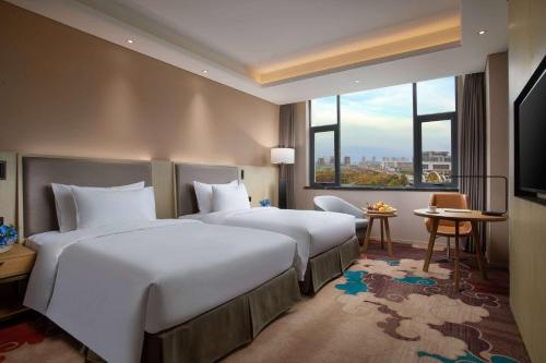 a hotel room with two beds and a large window at Ramada Wyndham Zhengzhou Xinzheng in Xinzheng