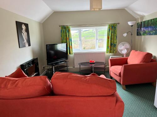 a living room with two red couches and a tv at Pentre Cerrig Country House in Llanferres