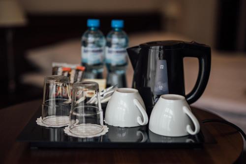 Hotel Rezydent في كراكوف: إبريق قهوة وأكواب على طاولة مع زجاجات مياه