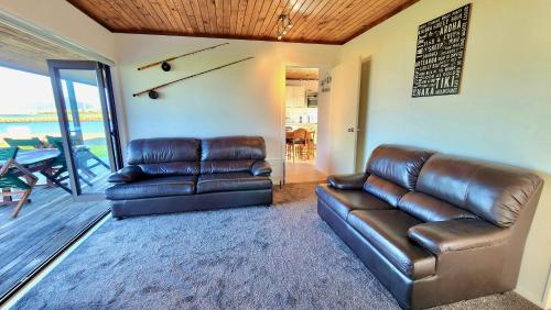 a living room with a leather couch and a table at The Sunrise Bach - One Tree Point Holiday Home in One Tree Point