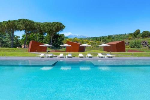 a swimming pool with white chairs and umbrellas at Tenuta della Contea in Mascali