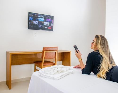 a woman sitting on a bed holding a remote control at Hotel Acarau Riviera in Acaraú