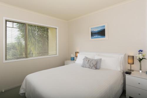 a white bedroom with a white bed and a window at Seascape Villa B&B in Tauranga