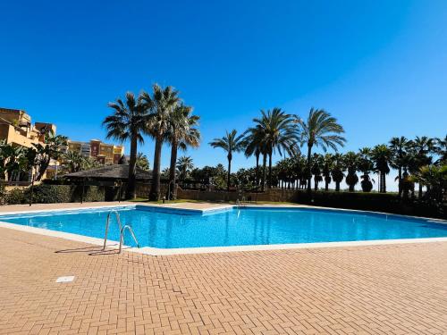 a large swimming pool with palm trees in the background at Los Jardines Isla Canela in Huelva