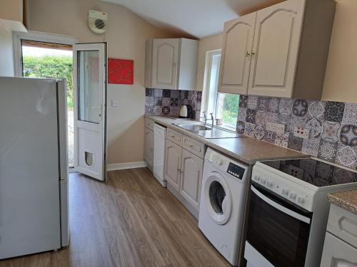 a kitchen with white cabinets and a washer and dryer at Bogrie Cottage in Canonbie