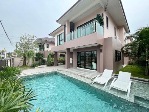 a house with a swimming pool and two white chairs at Southern Peak Pool Villa Huay Yai Pattaya in Ban Huai Yai