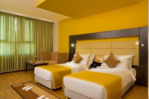 two beds in a hotel room with yellow walls at Poppys Hotel Madurai in Madurai