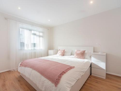 a white bedroom with a large bed with pink pillows at Pass the Keys Stylish 2 Bedroom Family Home in Worcester Park