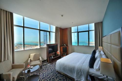 a hotel room with a bed and a tv and windows at Ramada Abu Dhabi Corniche in Abu Dhabi