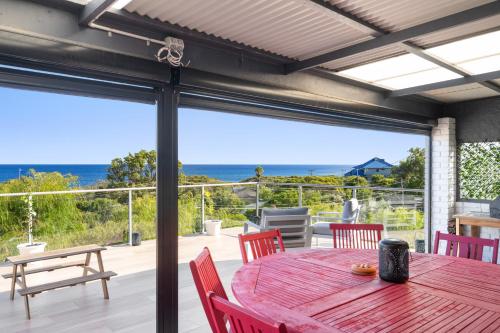 a red table and chairs on a patio with a view of the ocean at Oceanview Manor by "Peppy Beach Retreats" - Two Houses in One with Panoramic Views in Capel