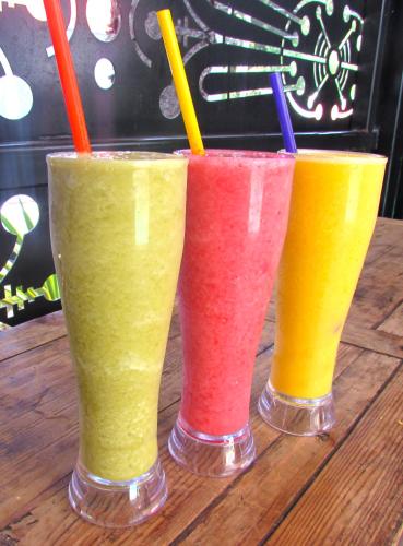 three different colored drinks sitting on a wooden table at Medellín Vibes Hostel in Medellín
