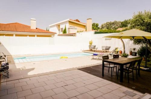 um pátio com uma mesa e um guarda-sol ao lado de uma piscina em Villa Ramiro em Azeitao