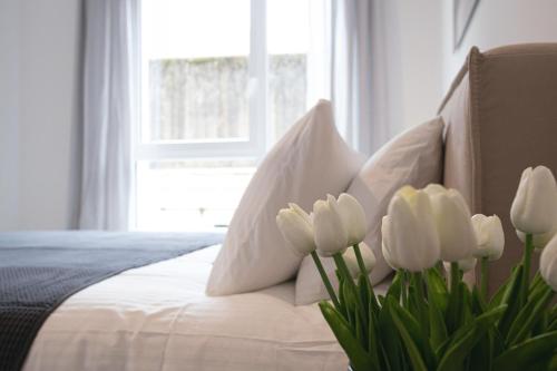 a white bed with white tulips in front of a window at Origer Apartments by Rentaroo in Luxembourg