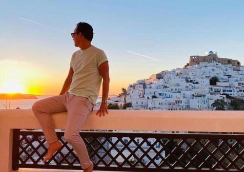 a man sitting on a bench with a view of a city at Kallichoron Art Boutique Hotel in Astypalaia Town