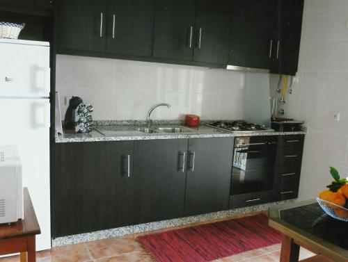 eine Küche mit schwarzen Schränken, einer Spüle und einem Kühlschrank in der Unterkunft Casa Quelhas in Besteiros