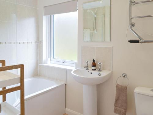La salle de bains blanche est pourvue d'un lavabo, d'une baignoire et de toilettes. dans l'établissement Fernilea Cottage, à Carbost