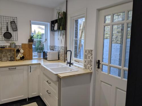 a kitchen with white cabinets and a sink and windows at Beautiful seaside Willow Cottage hosted by Whitstable-Holidays in Whitstable