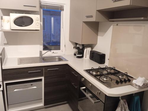 a small kitchen with a stove and a sink at Joli mobil-home pour 8 personnes tout confort 3 chambres vue étang avec piscine in Onzain