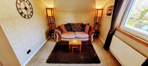 a living room with a couch and a clock on the wall at Self catering upper floor flat at Woodend house in Balmacara